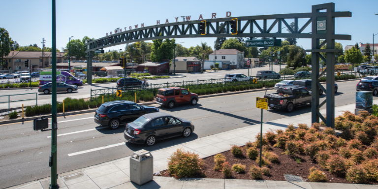Photo of Mission Boulevard, a two way street with three lanes on each side and a large arching sign reading Downtown Hayward.