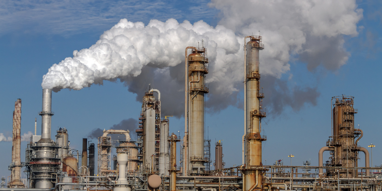 Photo of a petroleum factory with smoke billowing out of smokestacks.