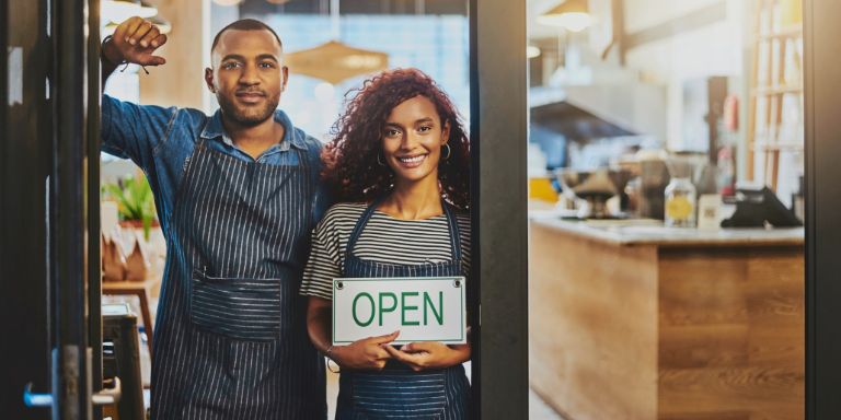 A couple standing in front of a newly opened business with an open sign