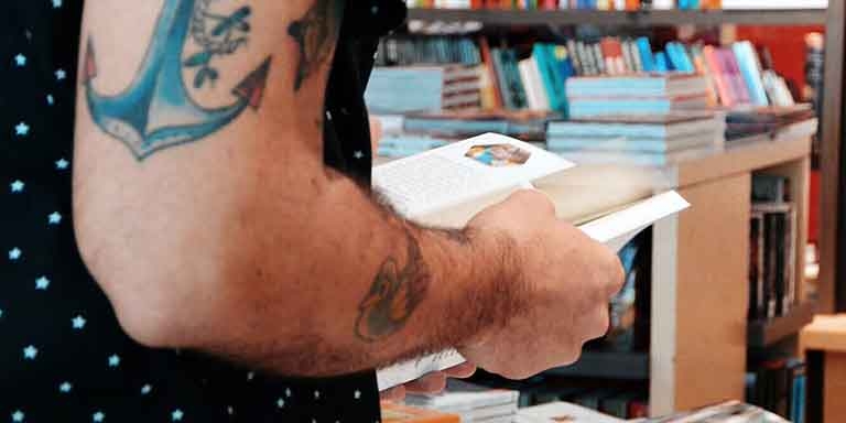A person with a tattooed arm holding a book in the library