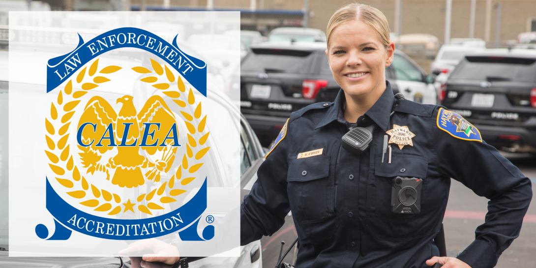A police officer smiling standing next to a police car. The Yellow and blue CALEA logo is to the left of the officer.