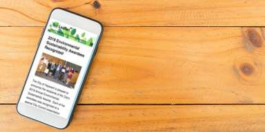 White cellphone on a wooden table showing The Leaflet Newsletter on the screen