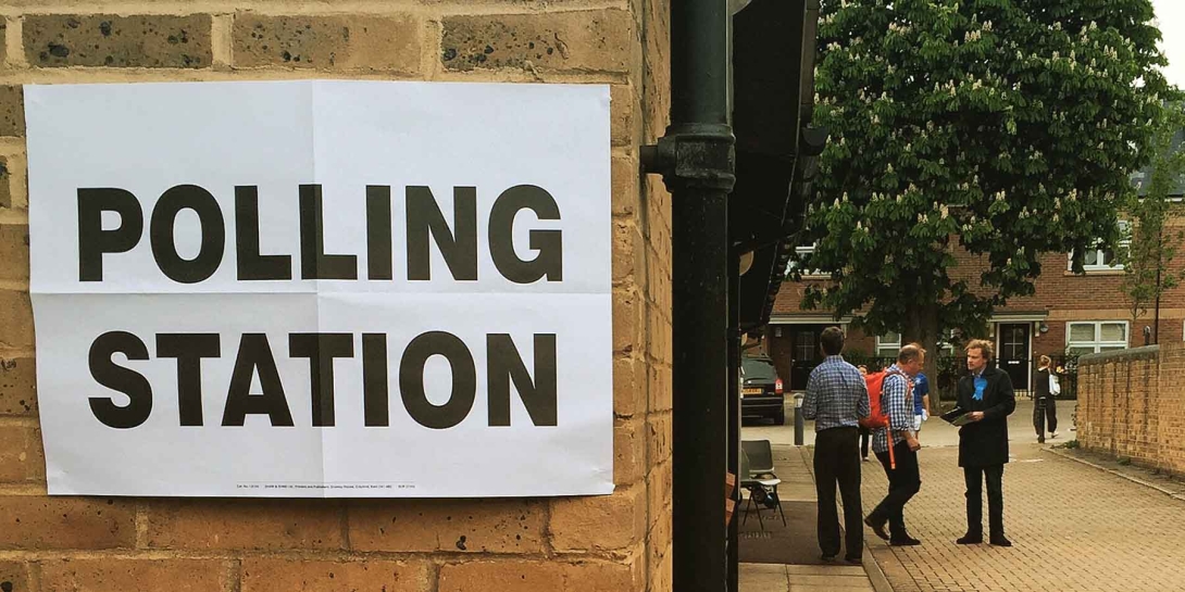 A white polling station sign on the side of a building